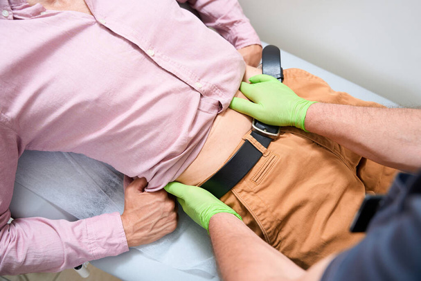Experienced therapist palpates the patients abdomen, the doctor works wearing protective gloves - Photo, Image