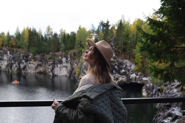 portrait of a beautiful young woman with freckles in a hat on the background of a lake surrounded by trees. - Foto, imagen