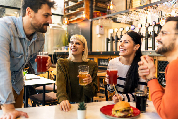 Glimlachende jonge vrienden drinken ambachtelijk bier in pub - Foto, afbeelding