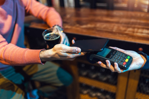 Людина в барі, що платить за допомогою мобільного пристрою - Фото, зображення