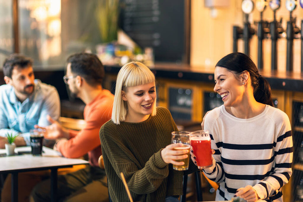 Uśmiechnięci młodzi przyjaciele pijący piwo rzemieślnicze w pubie - Zdjęcie, obraz