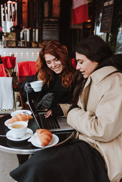 Ισπανοί επιχειρηματίες ζευγάρι γυναικών που εργάζονται και χρησιμοποιούν φορητό υπολογιστή σε καφετέρια το χειμώνα σε μια αστική πόλη στην Ευρώπη - Φωτογραφία, εικόνα