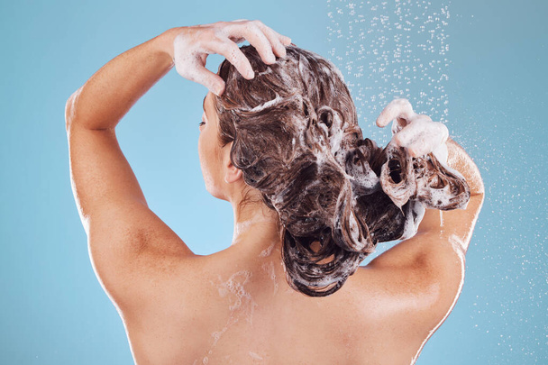 Woman, back and shampoo, haircare in shower and hygiene with water drops on blue background. Grooming, cosmetic care and sustainability, female person and morning routine, soap or foam in hair. - Zdjęcie, obraz