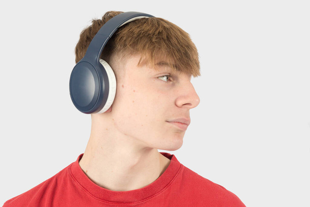 Kaukázusi 15 éves tinédzser fiú, piros pólóban, zenét hallgat fülhallgatón keresztül, oldalra néz. - Fotó, kép