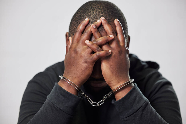 Handcuffs, arrested criminal and black man with stress, worry and anxiety in police station for crime. Law, punishment and male person with chains for investigation, theft and fraud suspect in prison. - Photo, Image
