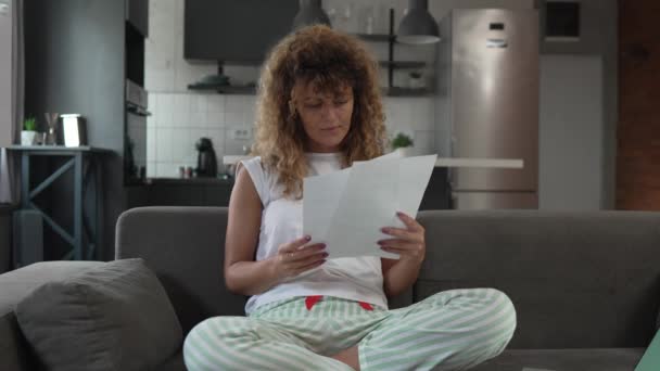 une femme caucasienne étudier à la maison lire et préparer l'examen de vraies personnes détiennent des documents papier ou du courrier tout en s'asseyant sur le canapé-lit  - Séquence, vidéo