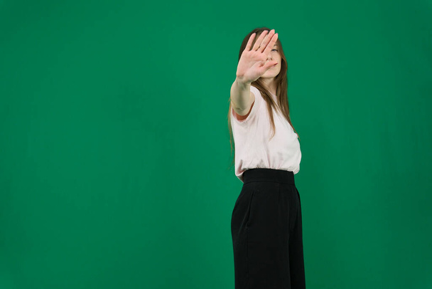 hand gesture stop different emotions of a young girl on a green background chromakey beautiful facial features real people pink T-shirt white skinned European. black flared wide leg trousers - 写真・画像