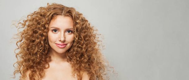 Vörös hajú nő hullámos hajjal és természetes sminkkel. Divatmodell hosszú göndör frizura és friss, tiszta bőr pózol fehér háttér - Fotó, kép