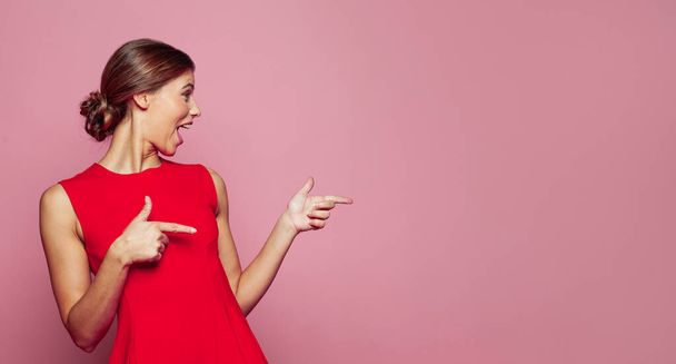 feliz bela mulher apontando dedo contra rosa estúdio parede banner fundo  - Foto, Imagem