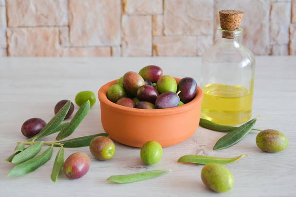 Фон из незрелых зеленых оливок и оливкового масла в деревянной тарелке - Фото, изображение