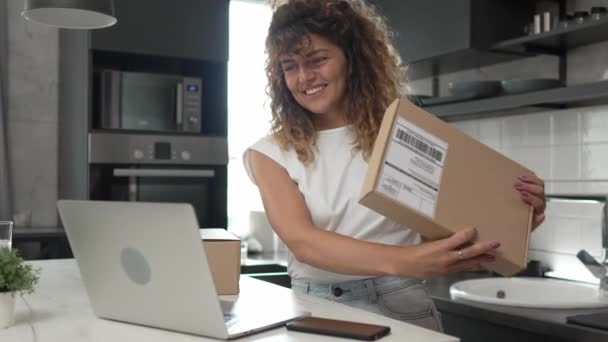 μία γυναίκα καυκάσια ενήλικη γυναίκα λαμβάνει δώρα σε κουτί ανοικτή διαβασμένη κάρτα χαρούμενο χαμόγελο μπροστά από φορητό υπολογιστή στο σπίτι έχοντας σε απευθείας σύνδεση βίντεο κλήση αργή κίνηση - Πλάνα, βίντεο