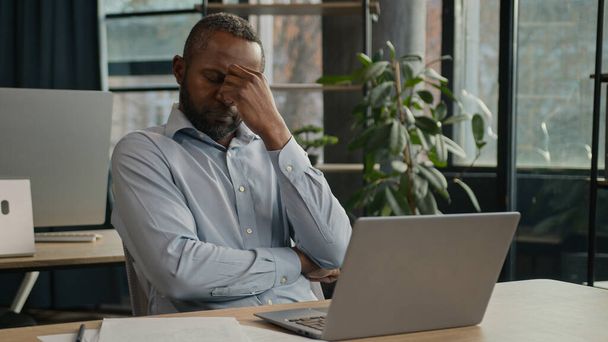 Exhausted sick mature senior businessman tired African American ethnic man office executive work on computer typing feel headache pain eyestrain fatigue health problem suffer migraine ache sit indoors - 写真・画像