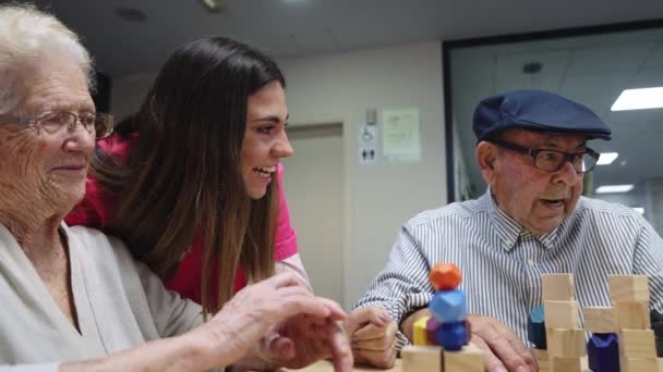 Video van een gelukkige verpleegster en oude mensen glimlachend tijdens het spelen van vaardigheidsspelletjes in een verpleeghuis - Video