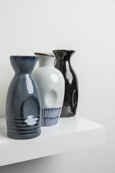 Malé dekorativní porcelánové vázy modré, bílé a černé barvy na bílé dřevěné polici - Fotografie, Obrázek