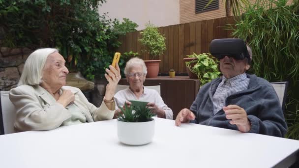 Vídeo de idosos usando óculos de realidade virtual sentados em um jardim em um lar de idosos - Filmagem, Vídeo