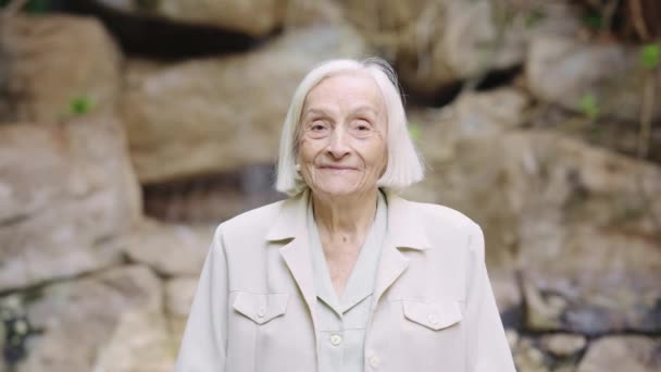 Video van een oude vrouw glimlachend naar de camera buiten in een verpleeghuis - Video