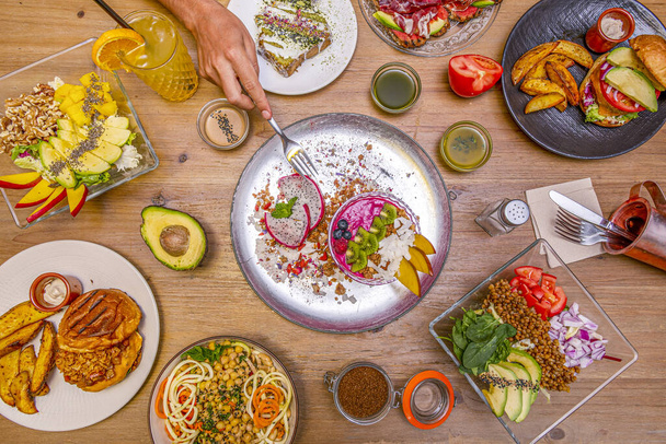 Mooie set gezonde, veganistische gerechten, salades en desserts met een hand die een vork vasthoudt - Foto, afbeelding