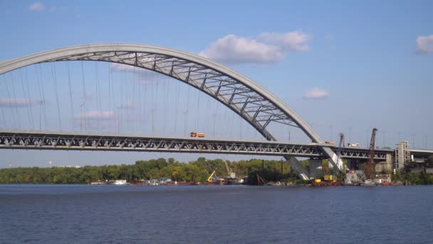 Podolszkij híd építése Kijevben. Teherautók vezetnek a hídon. Építőipari daruk állnak a folyóban a part közelében - Felvétel, videó