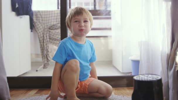 Een jongetje zit op de vloer voor een raam. - Video