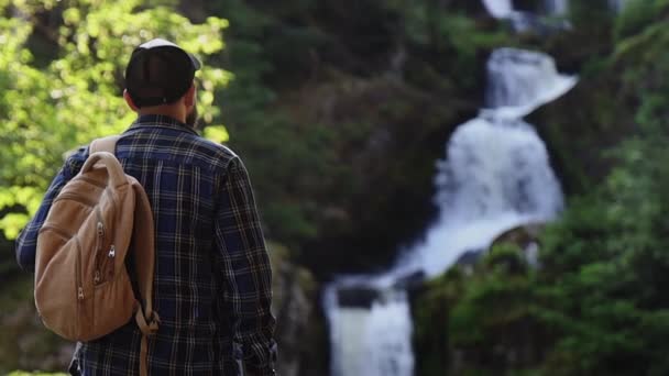 człowiek podziwia górski krajobraz i wodospad - Materiał filmowy, wideo