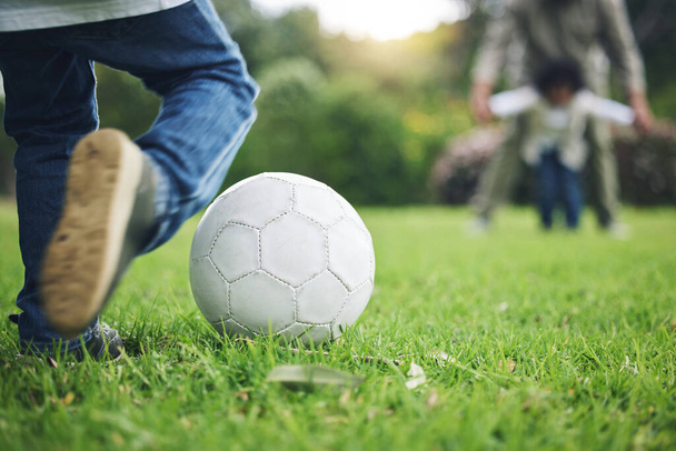 Παιδί, πόδια και κλωτσιά μπάλα ποδοσφαίρου στο γρασίδι για διασκέδαση, παιδική ηλικία ή παίζοντας στο πάρκο. Παιχνιδιάρικο αγοράκι σε αθλητικό παιχνίδι ή αγώνα για σκορ, πόντο ή γκολ στο πράσινο πεδίο στην ύπαιθρο της φύσης. - Φωτογραφία, εικόνα