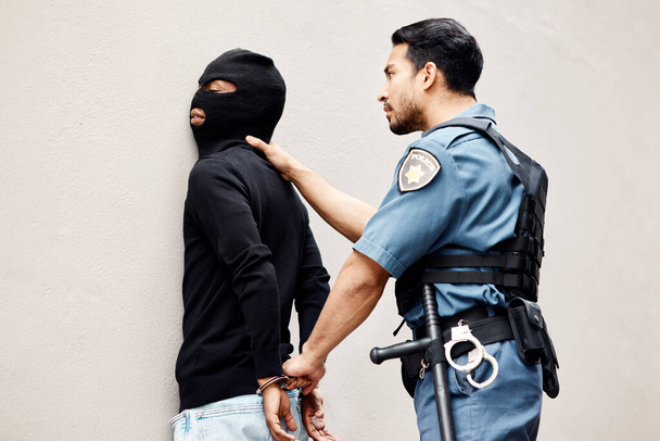 Man, police and handcuffs on gangster for arrest, crime or justice in theft, robbery or violence. Male person, officer or security guard cuffing hands of robber, thief or criminal against the wall. - Photo, Image