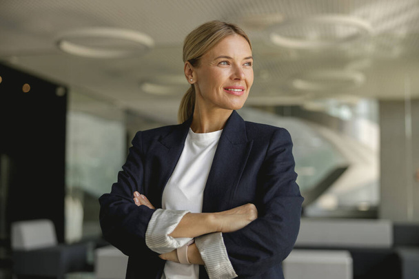 Portret uśmiechniętej kobiety przedsiębiorcy z skrzyżowanymi rękami stojącej na stanowisku i odwracającej wzrok - Zdjęcie, obraz