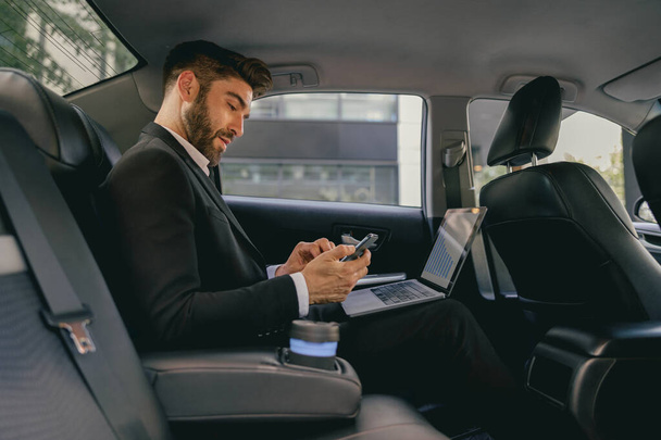 Schöner Geschäftsmann im Anzug mit Personal Computer und Handy im Taxi - Foto, Bild