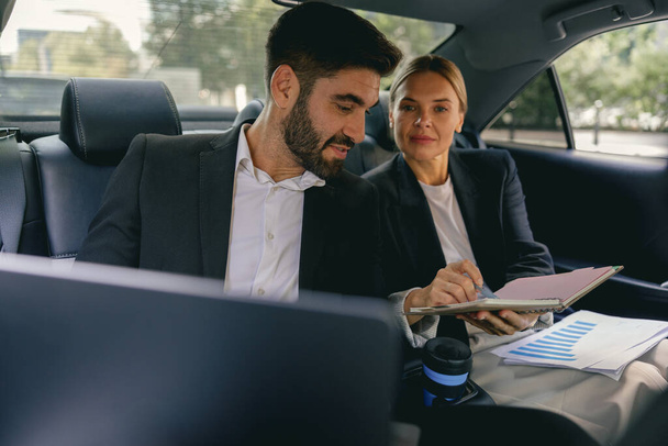 Gut gelaunte Geschäftsleute treffen sich online per Laptop, während sie auf den Rücksitzen im Auto sitzen - Foto, Bild