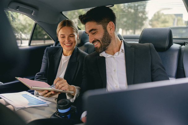 Vrolijke zakenmensen hebben online vergadering met behulp van laptop terwijl zitten in de auto achterbank - Foto, afbeelding