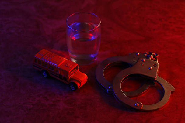Verre avec boisson alcoolisée vodka, menottes et bus scolaire jaune. Criminalité scolaire et alcoolisme concept - Photo, image