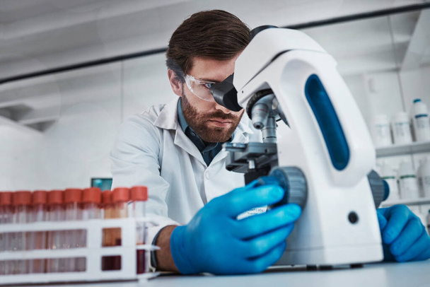Trabajando en laboratorio, el hombre estudiando ADN químico en tubo de ensayo y la investigación biotecnológica científica en Alemania. Científico de patología, solución líquida y microscopio se centran en la carrera en ciencias médicas. - Foto, Imagen