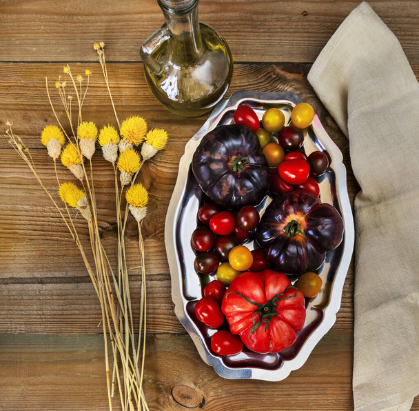 A still life of delicious ripe tomatoes inside a metal tray next to some dried yellow flowers - Photo, Image