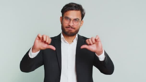 Не подобається. Невдоволений індійський бізнесмен показує великі пальці вниз жест, висловлюючи невдоволення, невдоволення, незадоволені негативні відгуки. Привабливий чоловік в приміщенні ізольований на сірому фоні - Кадри, відео