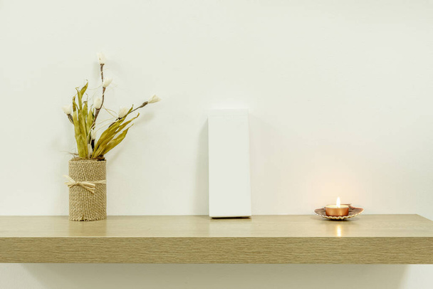 Легка дубова імітація дерев'яної полиці з білим картонним пакетом, орнаментом сухих квітів і невеликою запаленою свічкою
 - Фото, зображення