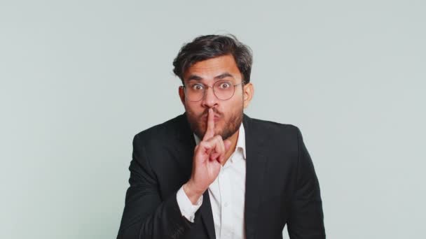 Silencio, por favor. Empresario indio presiona dedo índice a los labios hace gesto de silencio signo no dice secreto, dejar de hablar chismes, privacidad confidencial. Hombre árabe aislado sobre fondo gris - Imágenes, Vídeo
