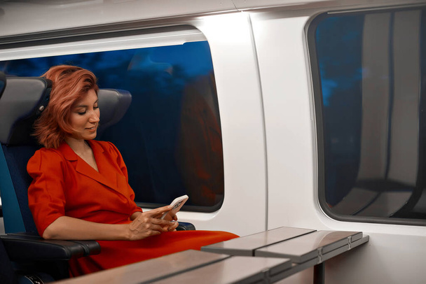 女性は,電車の交通機関でモバイルスマートフォンで旅行し,彼女のソーシャルメディアをチェックし,別の都市での旅行に関するウェブサイトやインターネット情報を読みます. 高速都市電車を満喫する遅延なし - 写真・画像