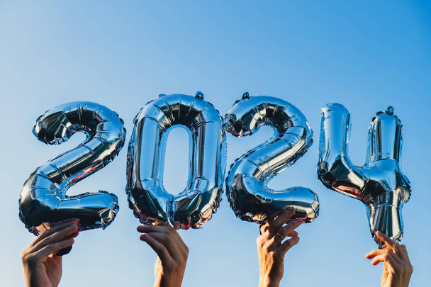 Feliz año nuevo 2024 globos metálicos sobre fondo azul cielo. Tarjeta de felicitación plata foil globos números Navidad concepto de vacaciones. Celebración fiesta de felicitación decoración - Foto, Imagen