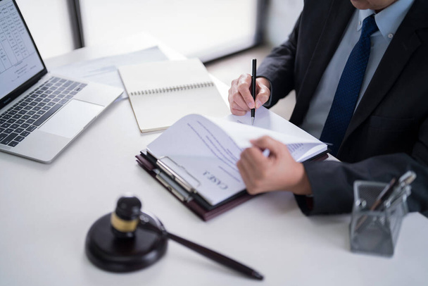 Male lawyer reading and checking financial document of business to analysis about legal agreement and terms of business contract while working on the desk with laptop technology in law firm. - Photo, Image