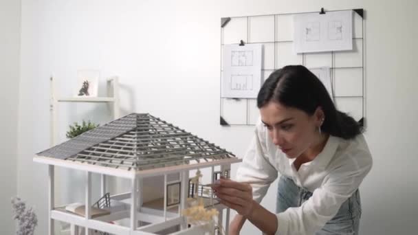 Detailní záběr mladé krásné inteligentní inženýrky se zaměřuje na měření modelu domu pomocí tužky v moderní kanceláři s nákresem svlečeným na stěně. Tvůrčí koncept bydlení a designu. Neposkvrněné. - Záběry, video