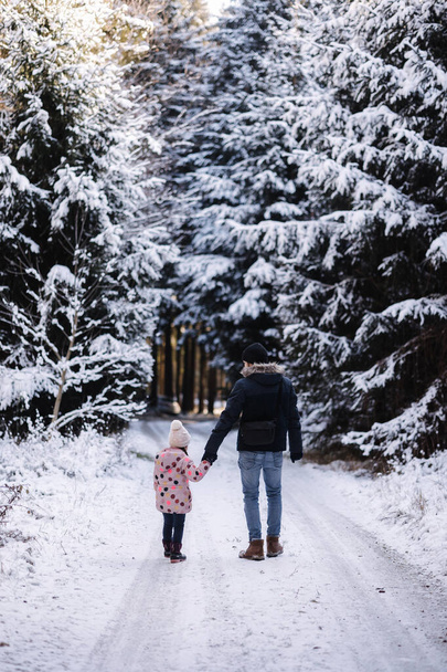 Imádnivaló kislány, aki az apjával sétál a havas erdőben. Apa és a lánya együtt töltenek egy kis időt a karácsonyi szünetben. Kiváló minőségű fénykép - Fotó, kép