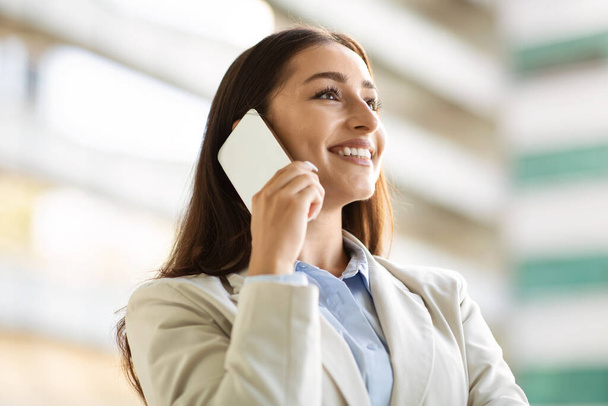 Happy pretty confident young european woman in suit enjoy work, call by smartphone in city outdoors, close up. Business, startup, communication and lifestyle, ad and offer - Photo, Image