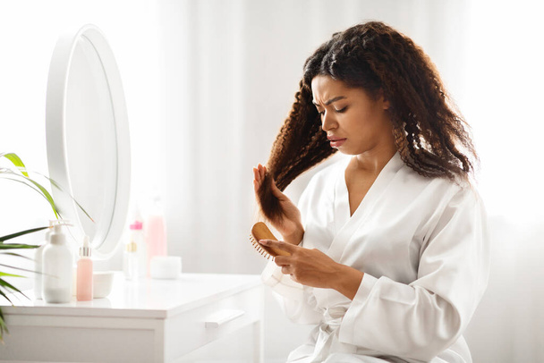 Upset Black Woman Irritated By Tangled Hair, Using Bamboo Brush At Home, Unhappy African American Female Suffering Painful Feeling, Looking At Split Dry Ends And Frowning While Combing Her Curly Hair - Zdjęcie, obraz