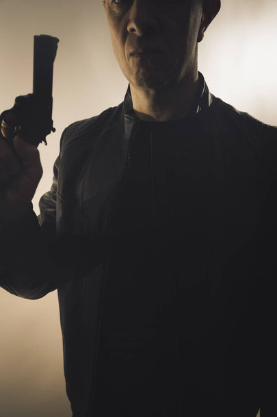 Ντετέκτιβ κατάσκοπος θρίλερ άνθρωπος με όπλο φωτογραφία σκούρο στούντιο πυροβόλησε με κινηματογραφικό φωτισμό. - Φωτογραφία, εικόνα