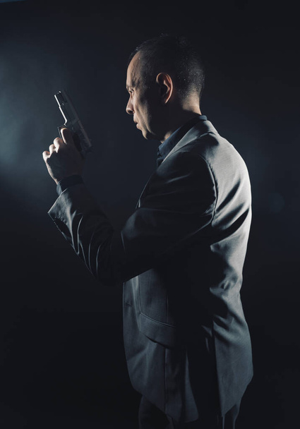Spy σε κομψό κοστούμι με πιστόλι σε σκούρο στούντιο πυροβόλησε φωτογραφία με απλό φόντο και να αντιγράψετε χώρο. - Φωτογραφία, εικόνα
