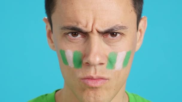 Video im Studio mit Chroma der Nahaufnahme eines ernsten Mannes mit einer nigerianischen Flagge im Gesicht, der in die Kamera blickt - Filmmaterial, Video