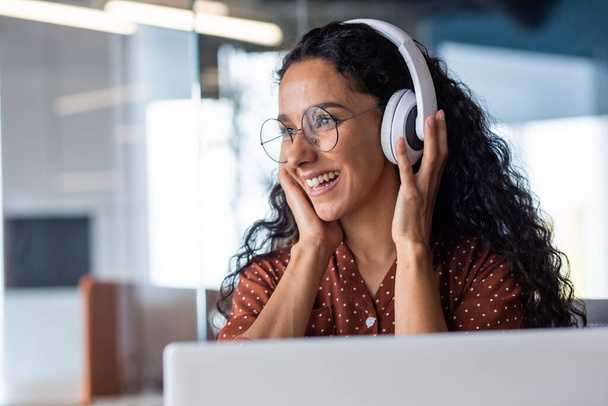 Young beautiful woman working in the office at the workplace, close-up hispanic woman in headphones singing along and dancing joyfully, business woman on break resting, programmer happy. - Photo, Image