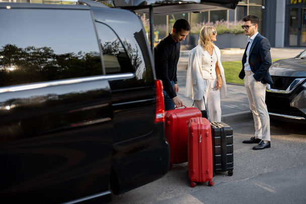 Coppia di uomini d'affari in piedi accanto a un taxi in attesa del loro autista o portiere per aiutarli con una valigia. Concetto di viaggi d'affari e di viaggio - Foto, immagini
