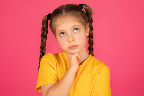 Portrait Of Thoughtful Little Girl Touching Chin And Looking Up, Closeup Shot Of Pensive Preteen Female Child Standing Isolated Over Pink Studio Background, Considering Options, Planning Something - Photo, Image