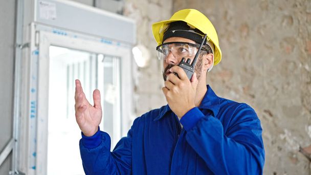 Jonge Spaanse man aan het praten op walkietalkie op bouwplaats - Foto, afbeelding